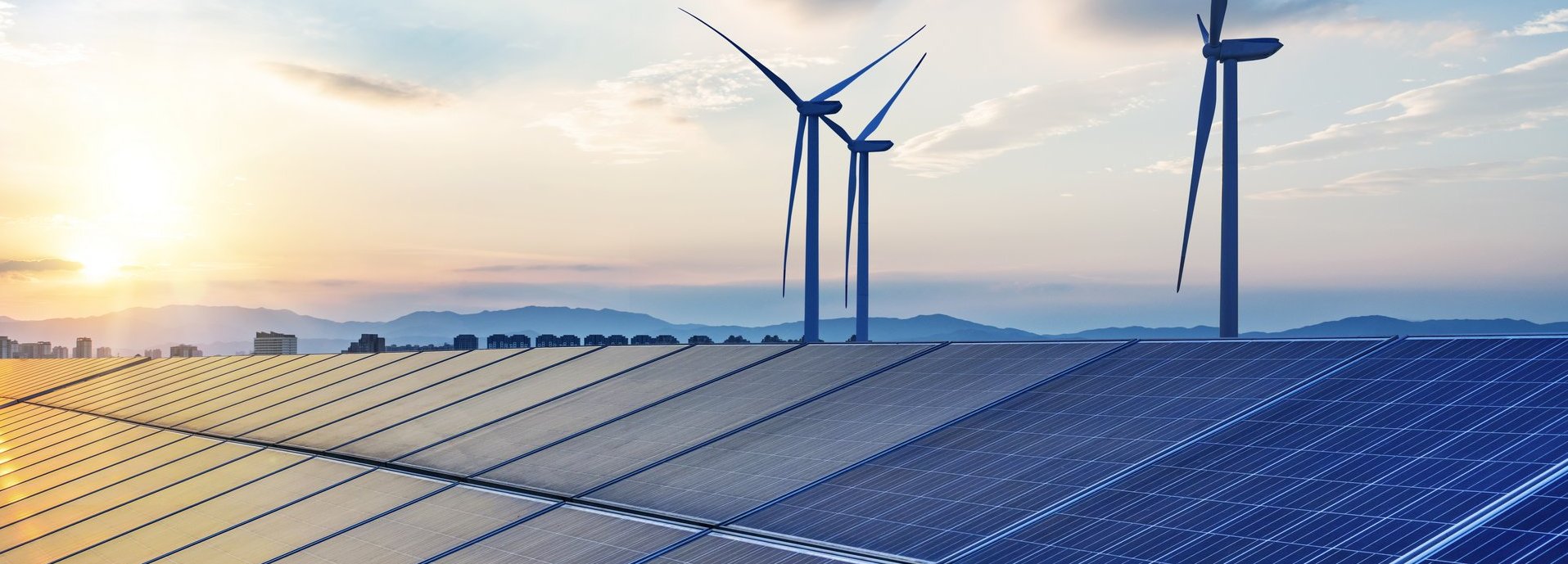 Solarkollektoren mit Windrädern im Hintergrund vor blauem, wolkenbehangenem Himmel