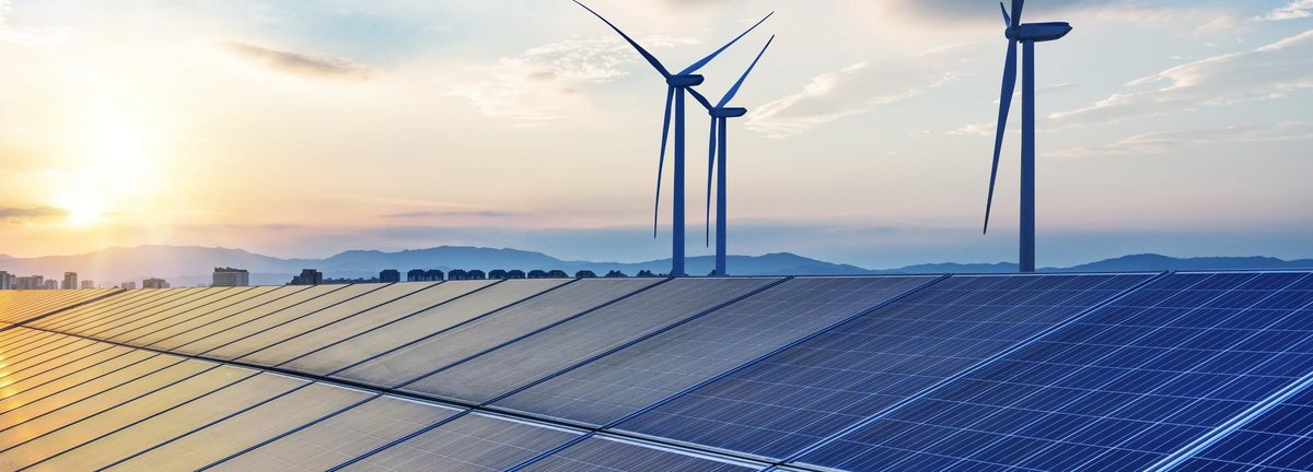 Solarkollektoren mit Windrädern im Hintergrund vor blauem, wolkenbehangenem Himmel