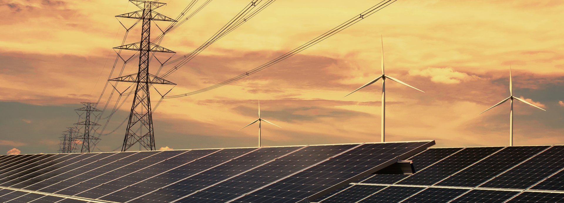 Strommasten, Solarkolelktoren und Windräder vor orangenem Himmel mit Sonnenuntergang