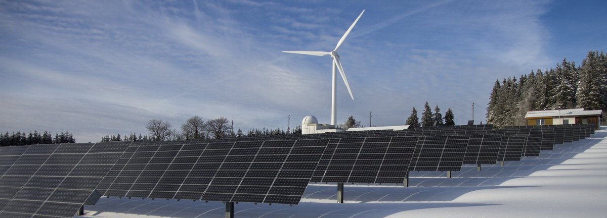 Solaranlagen und ein Windrad im Hintergrund im Winter auf schneebedecktem Feld