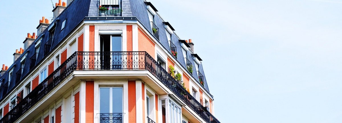 Wohnhaus mit rot weißer Fassade und blauem Dach und Balkons vor einem hellblauen Himmel