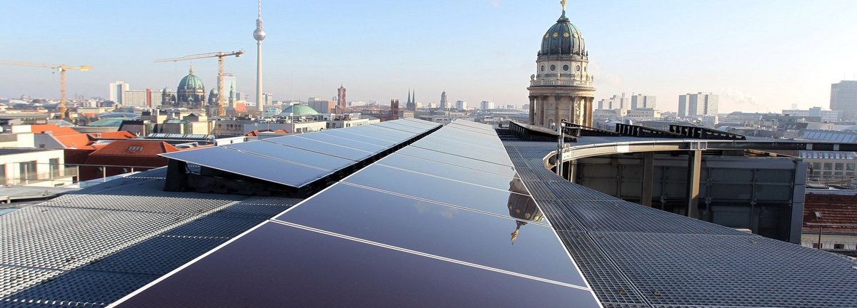 Solarzellen auf einem Dach in Berlin mit dem Fernsehturm am Horizont und blauem Himmel