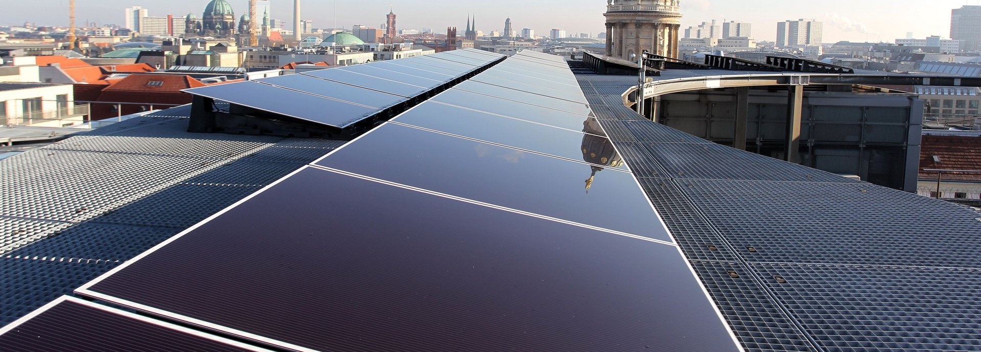 Solarzellen auf einem Dach in Berlin mit dem Fernsehturm am Horizont und blauem Himmel