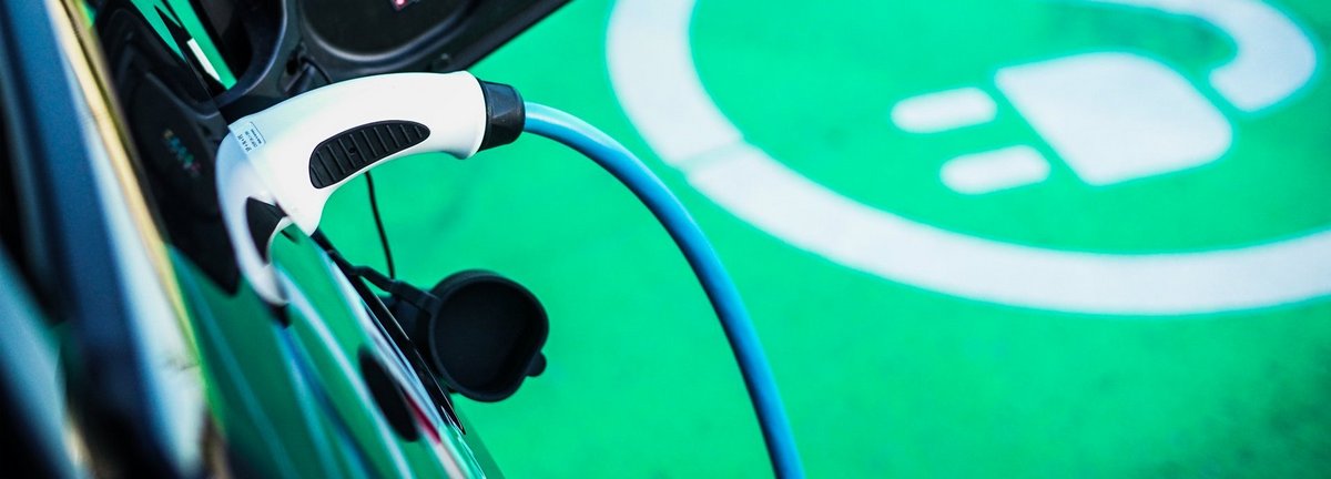 Nahaufnahme Elektroauto wird geladen auf einem grünen Teppich mit Stromsteckersymbol