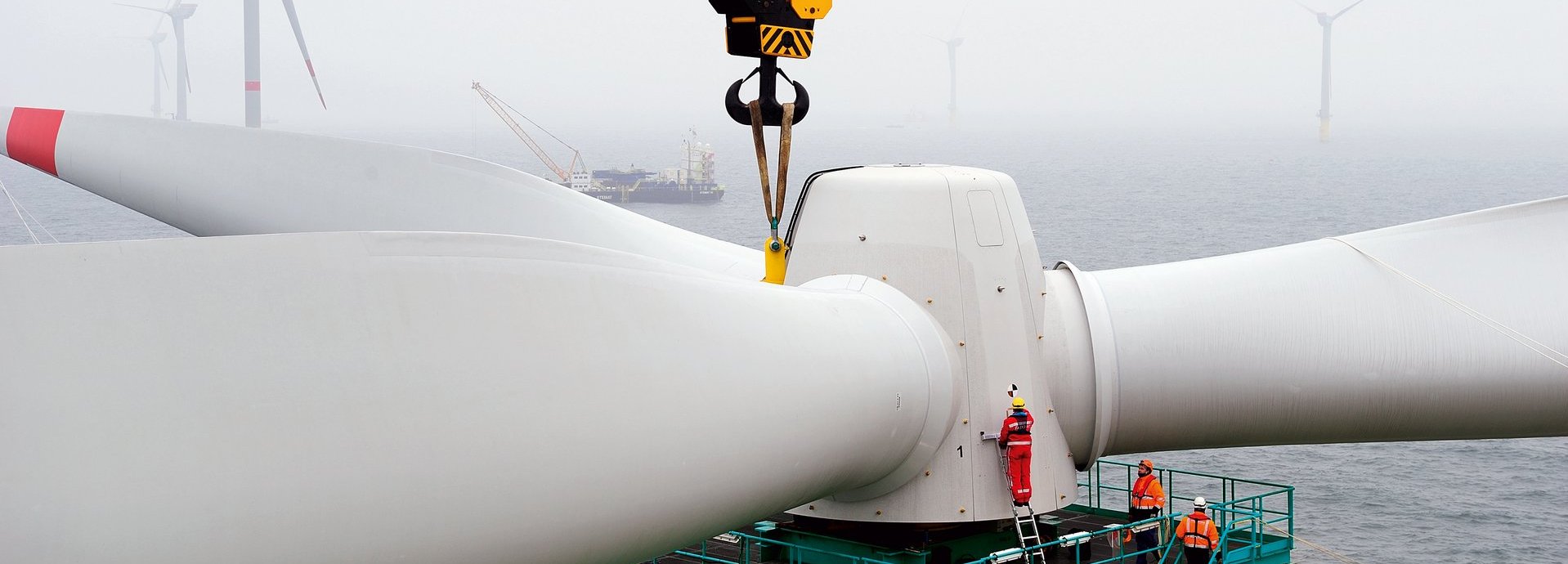 Turbine wird auf Offshore Windrad gebaut mit Kran und Arbeitern