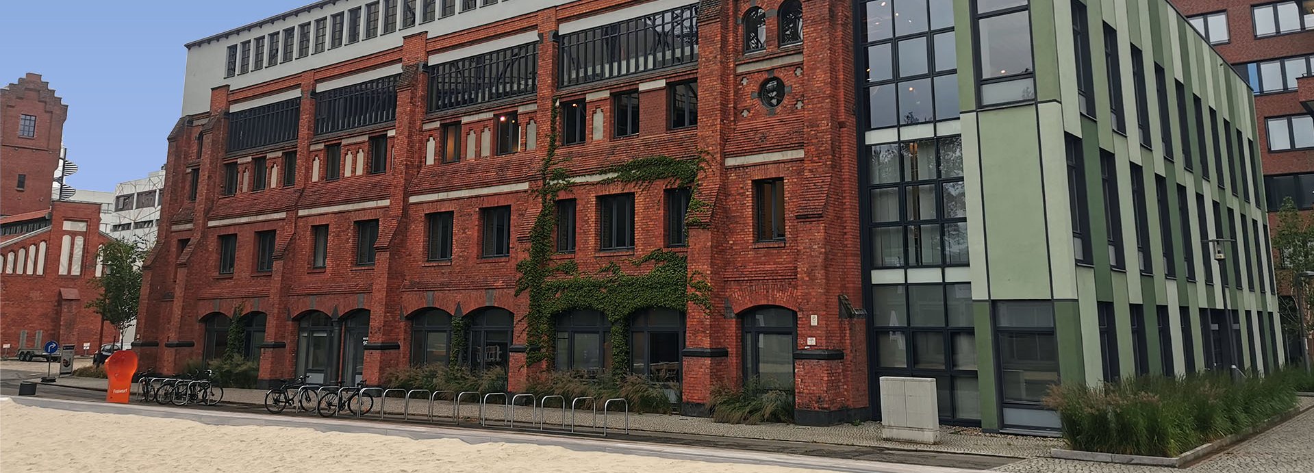 Haus 16 auf dem EUREF-Campus, Ziegelsteingebäude mit Volleyballfeld im Vordergrund