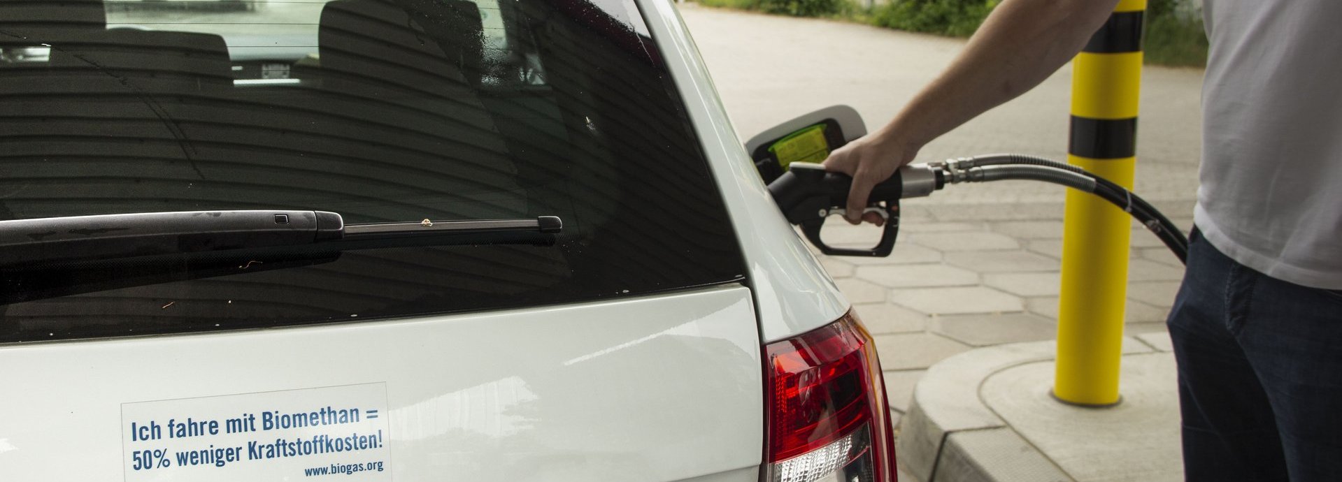 ich fahre mit Biomethan 50 prozent weniger kraftstoff Zeichen an einem weißen Auto das gerade geladen wird