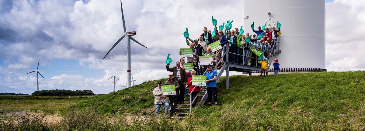 Menschengruppe mit Wir sind die Energiewende Schildern auf den Treppen vor einem Windrad