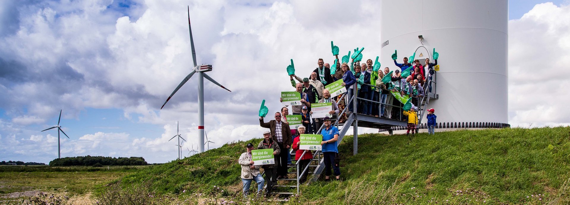 Menschengruppe mit Wir sind die Energiewende Schildern auf den Treppen vor einem Windrad