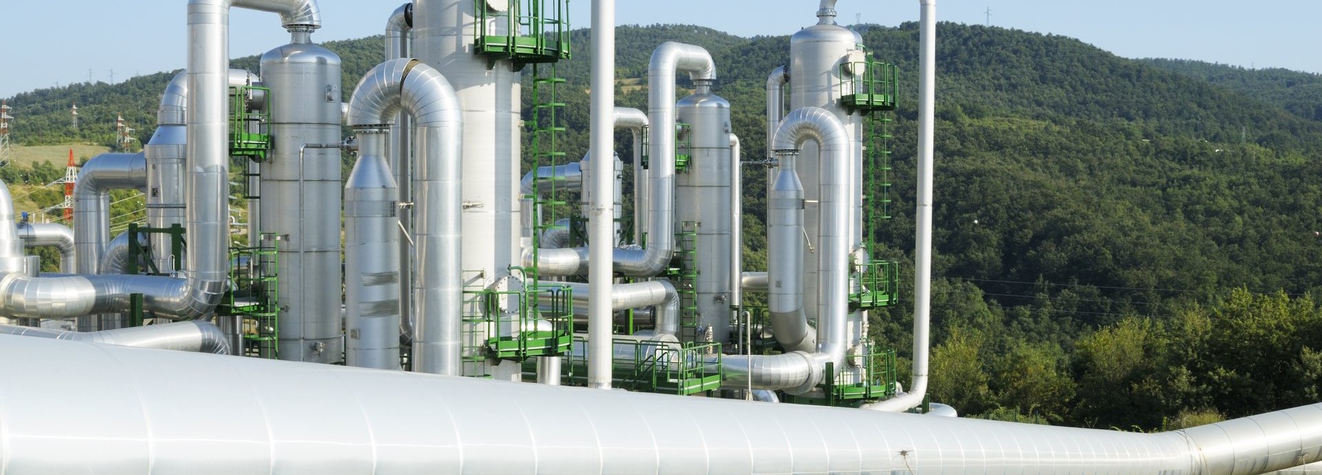 Geothermiekraftwerk in hügeliger grüner Landschaft mit Rohren