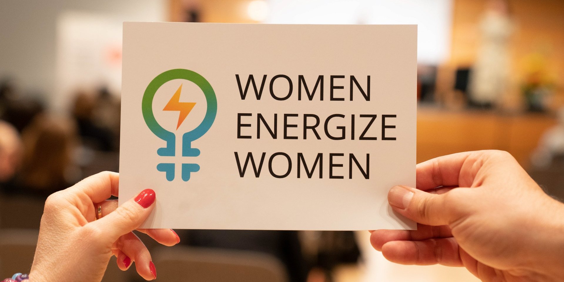 Schild mit Women Energize Women Logo wird hochgehalten 