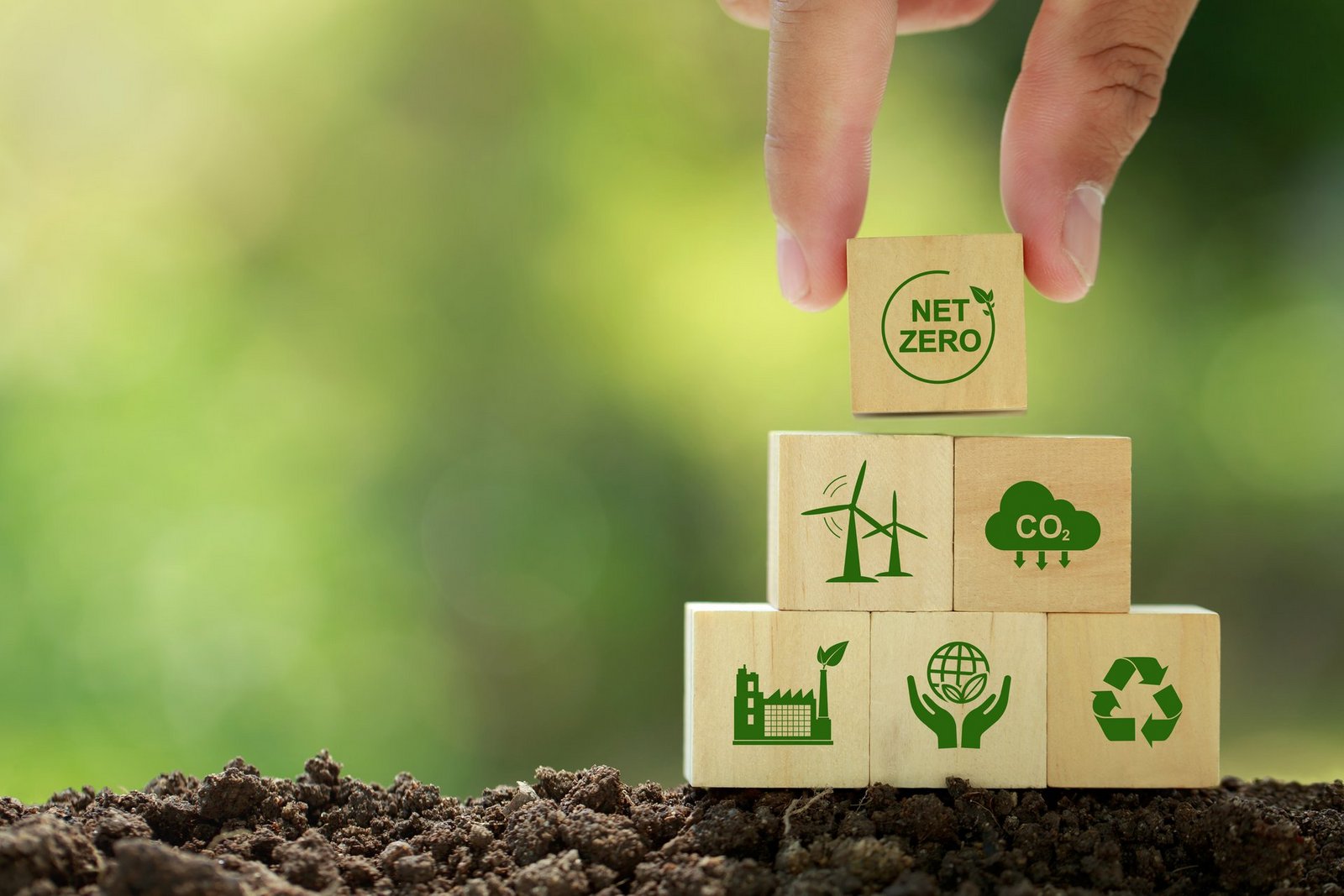 Netto-Null- und CO2-neutrales Konzept. Hand setzt Holzwürfel mit Netzero-Symbolen - erneuerbare Energie, CO2-Emissionsreduzierung, grüne Produktion, Abfallrecycling. auf grünem Hintergrund